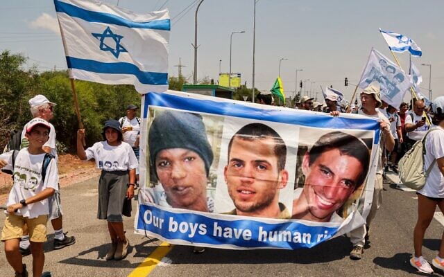 Demonstrators marching with a banner showing the faces of captive Israeli civilian Avera Mengistu, and late soldiers Oron Shaul and Hadar Goldin from the Israeli city of Ashkelon arrive at the Karmia kibbutz on August 5, 2022. (JACK GUEZ / AFP)