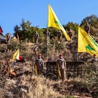 Hezbollah fighters pose with the terror group's flags (yellow) and flags bearing the names of venerated Shiite Muslim figures (black) during a ceremony to lay the foundation for a site for 'jihadist tourism,' at a camp formerly run by Iran's Islamic Revolutionary Guard Corps in Lebanon to train Hezbollah fighters, in the Janta region in the east of the country, on August 19, 2022. (AFP)