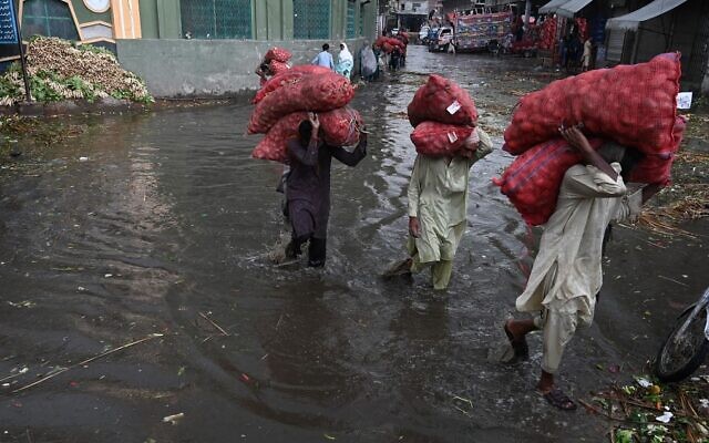 Pakistani laborers carry sacks of potatoes as they wade through a flooded market in Lahore on August 29, 2022. (Arif Ali/AFP) Pakistani laborers carry sacks of potatoes as they wade through a flooded market in Lahore on August 29, 2022. (Arif Ali/AFP)