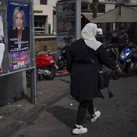 A woman walks by presidential campaign posters in Marseille, southern France, April 13, 2022 (AP Photo/Daniel Cole, File)