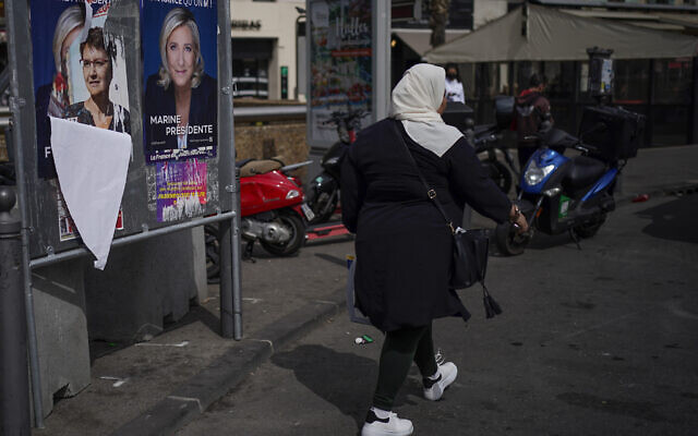 A woman walks by presidential campaign posters in Marseille, southern France, April 13, 2022 (AP Photo/Daniel Cole, File)