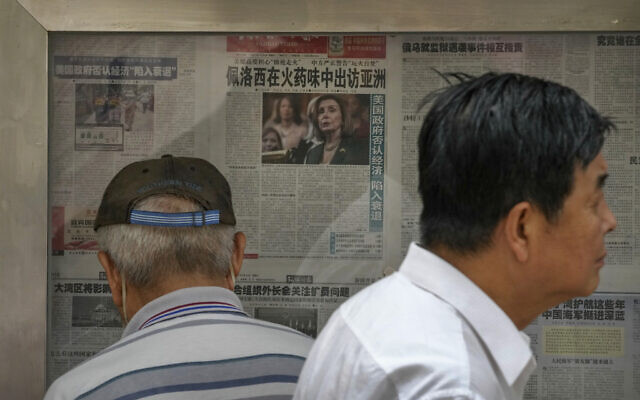 A resident walks by a man reads a newspaper reporting on US House Speaker Nancy Pelosi's Asia visit, at a stand in Beijing, July 31, 2022. (Andy Wong/AP)