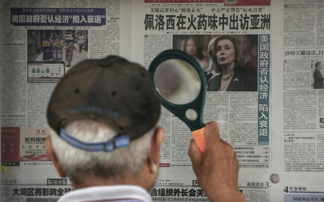 A man uses a magnifying glass to read a newspaper headline reporting on US House Speaker Nancy Pelosi's Asia visit, at a stand in Beijing, July 31, 2022. (AP Photo/Andy Wong)