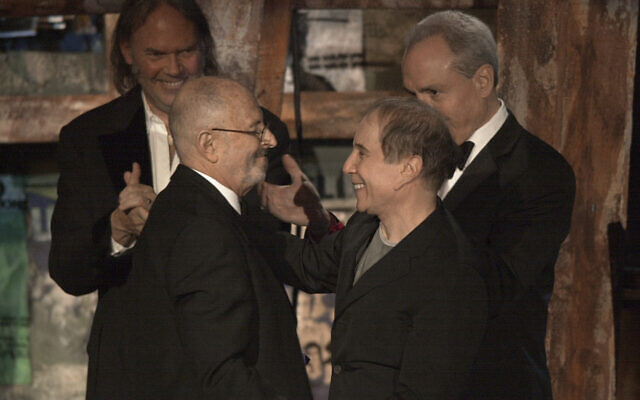 Record executive Mo Ostin, foreground left, is embraced by singer/songwriter Paul Simon, right, as singer/songwriter Neil Young, background left, and producer Lorne Michaels look on after Ostin was inducted into the Rock and Roll Hall of Fame in New York on March 10, 2003. (Gregory Bull/AP)