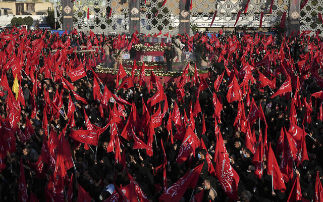 Mourners wave red flags as they gather around flag-draped coffins of five members of the paramilitary Revolutionary Guard killed in Syria, whose remains were recently recovered, during their funeral ceremony in Tehran, Iran, August 4, 2022. (AP/Vahid Salemi)