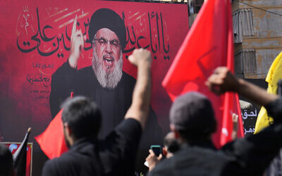 Hezbollah leader Sheik Hassan Nasrallah speaks via a video link, as his supporters raise their hands, during the Shiite holy day of Ashura, in the southern suburb of Beirut, Lebanon, August 9, 2022. (AP Photo/Hussein Malla)