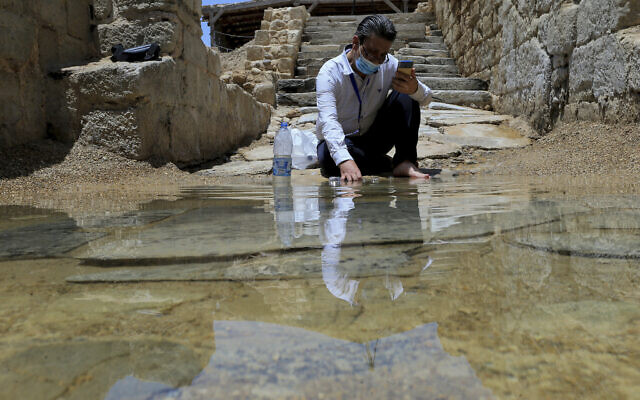Syrian Christian Zuhair Al-Sahawi immerses his hand in water at the Bethany Beyond the Jordan baptismal site on the east bank of the Jordan River in Jordan, June 8, 2022. (AP Photo/Raad Adayleh)