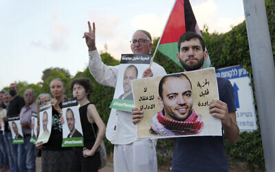 Protesters gather with a Palestinian flag outside the hospital in Be'er Yaakov where a hunger-striking security prisoner, Khalil Awawdeh, pictured in the placards, detained by Israel as an alleged terrorist, is in deteriorating health, August 13, 2022. Arabic on the placards reads, 'No administrative detention. Freedom for Khalil Awawdeh.' (AP/Tsafrir Abayov)