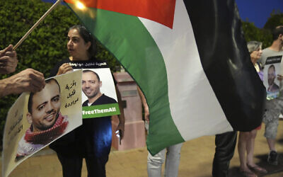 Protesters gather with a Palestinian flag outside a hospital in Be'er Yaakov where a hunger-striking security prisoner, Khalil Awawdeh, pictured in the placards, is in deteriorating health, August 13, 2022. (AP/Tsafrir Abayov)