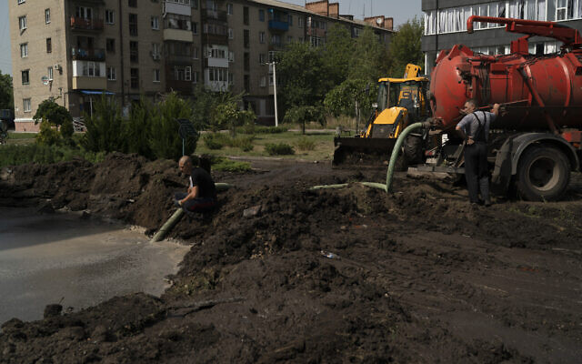Workers drain water from a crater created by an explosion that damaged a residential building after a Russian attack in Slovyansk, Ukraine, August 28, 2022. (AP/Leo Correa)