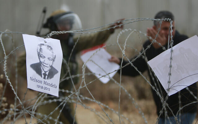 A portrait of late South African leader Nelson Mandela hangs on the wire fence as an Israeli soldier talks to a Palestinian protester during a weekly demonstration against Israel's separation barrier in the West Bank village of Bilin, near Ramallah, December 6, 2013. (AP Photo/Majdi Mohammed)