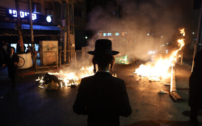 A protester watches as fires burn during a demonstration in Jerusalem on August 14, 2022, against the expected autopsy of a 4-year old boy. (Yonatan Sindel/Flash90)