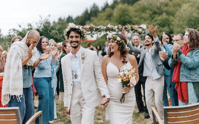 The bride and groom, Ophir Haberer and Adi Aboody, exit the chuppah after the ceremony with family and friends applauding, June 4, 2022. (Luna Munn Photography)