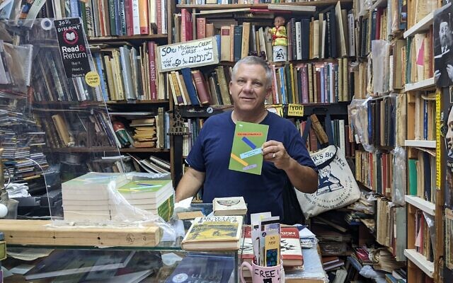 Yosef Halper, who used the pen name J.C. Halper in a nod to his American-born name, shows off his first published book in his Tel Aviv store on July 6, 2022. (Melanie Lidman/Times of Israel)