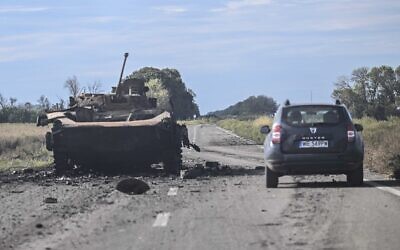A car drives past a destroyed Russian armored vehicle in Balakliya, Kharkiv region, on September 10, 2022, amid the Russian invasion of Ukraine. (Photo by Juan BARRETO / AFP)