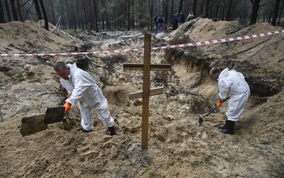 Two forensic technicians dig near a cross in a forest on the outskirts of Izyum, eastern Ukraine on September 16, 2022, after Ukrainian forces recaptured the eastern city from the Russians. (Juan Barreto/AFP)