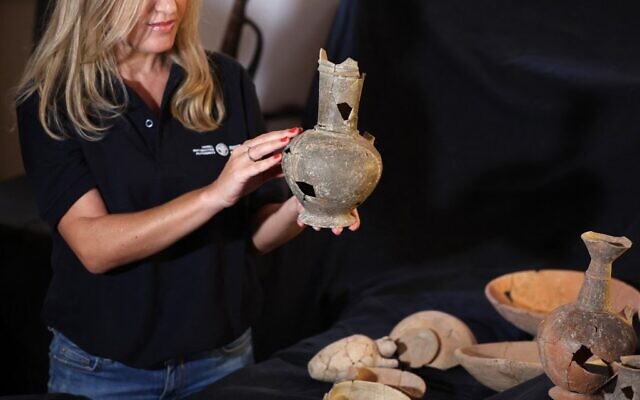 An employee at the Israel Antiquities Authority (IAA) holds one of the vessels that are believed to have contained opium in the 14th century BC, found at the Tel Yehud burial site and on display at the IAA offices in Jerusalem on September 20, 2022.(AHMAD GHARABLI / AFP)