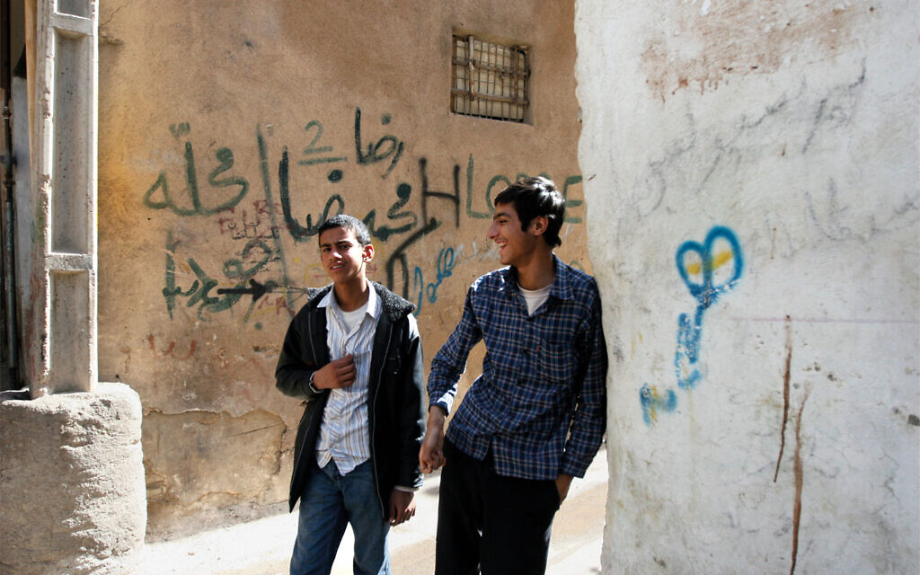 Two young men walk in a Jewish neighborhood in Shiraz. On the wall behind them, a derogatory term for Jews is written in graffiti. (Hassan Sarbakhsian/ via JTA)