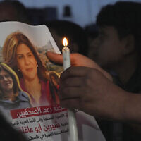 A Palestinian holds a light candle and a picture of slain Al Jazeera journalist Shireen Abu Akleh, to condemn her killing, in front of the office of Al Jazeera network, in Gaza City, May 11, 2022. (AP Photo/Adel Hana, File)