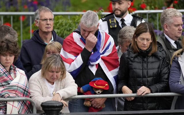 A person holding a Paddington Bear stuffed toy stands with members of the public outside Buckingham Palace waiting to watch Queen Elizabeth II funeral procession, in central London Monday, Sept. 19, 2022. The Queen, who died aged 96 on Sept. 8, will be buried at Windsor alongside her late husband, Prince Philip, who died last year. (AP Photo/Christophe Ena, Pool)