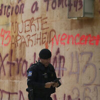 A security officer texts as he walks past the Israel's embassy that was defaced by demonstrators demanding the extradition of the former director of Mexico’s Criminal Investigation Agency, Tomas Zeron, who is accused of torture, forced disappearances and judicial misconduct in the case of the 43 missing students of Ayotzinapa, in Mexico City, Wednesday, Sept. 21, 2022. (AP Photo/Fernando Llano)