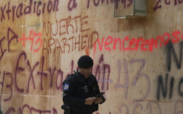A security officer texts as he walks past the Israel's embassy that was defaced by demonstrators demanding the extradition of the former director of Mexico’s Criminal Investigation Agency, Tomas Zeron, who is accused of torture, forced disappearances and judicial misconduct in the case of the 43 missing students of Ayotzinapa, in Mexico City, Wednesday, Sept. 21, 2022. (AP Photo/Fernando Llano)