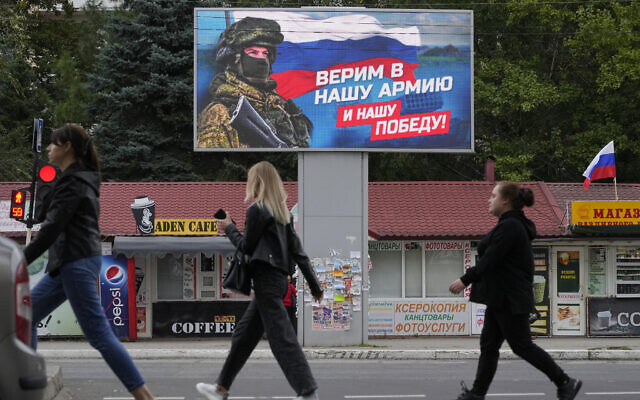 People walk past a billboard displaying a soldier and a Russian flag and reading 'We believe in our army and our victory' in Luhansk, Luhansk People's Republic controlled by Russia-backed separatists, eastern Ukraine, September 27, 2022. (AP Photo)