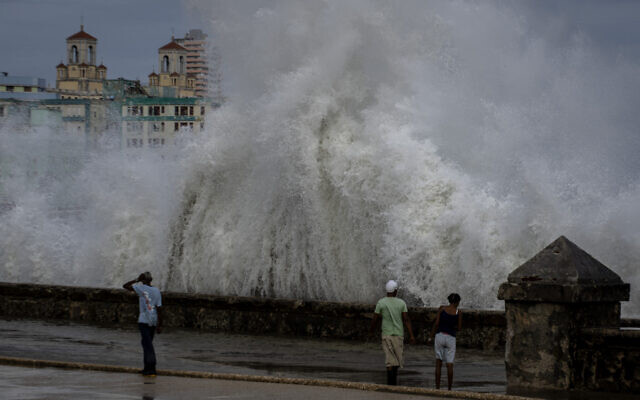 People stand along a waterfront as huge waves crash against a seawall in the wake of Hurricane Ian in Havana, Cuba, September 28, 2022. (AP Photo/Ramon Espinosa)