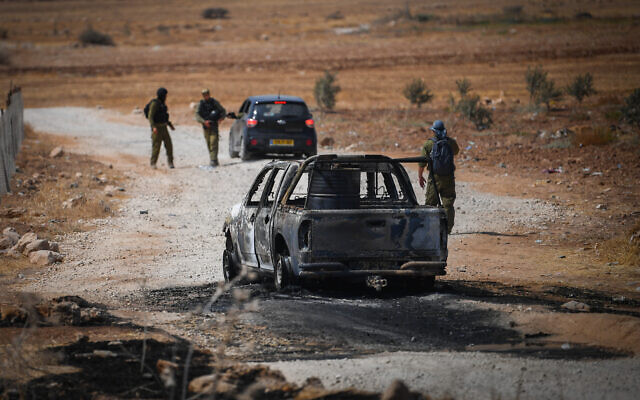Israeli security forces stand next to a burnt car allegedly used by the suspects who carried out a shooting attack on a bus in the Jordan Valley, September 4, 2022. (Flash90)