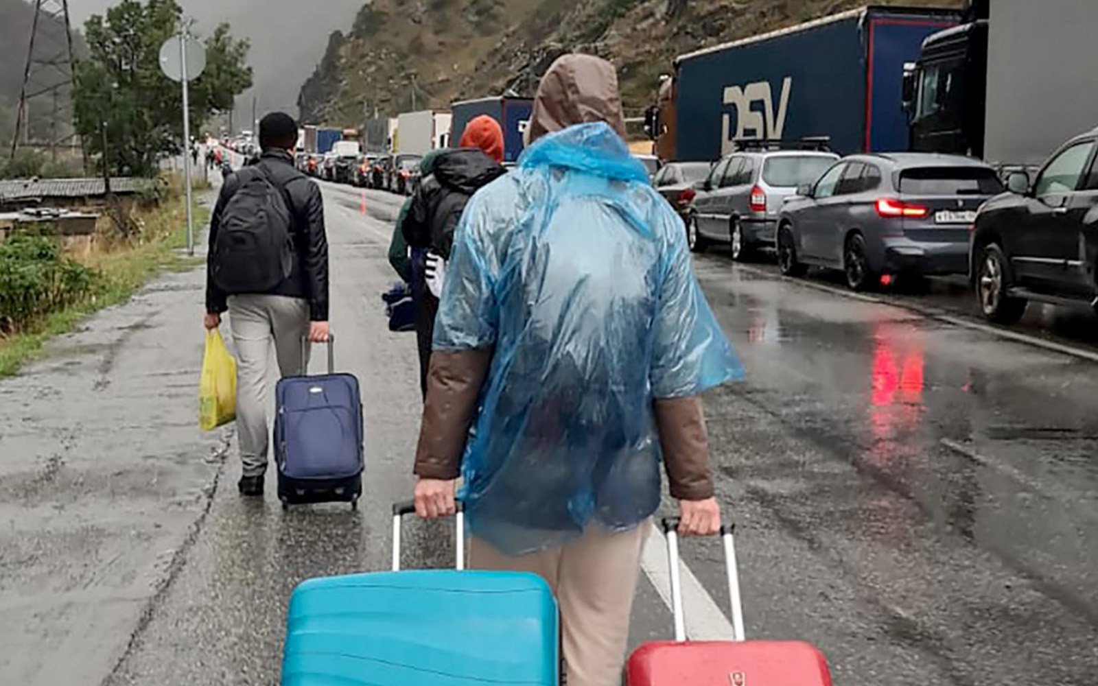 People carrying luggage walk past vehicles with Russian license plates on the Russian side of the border toward the Nizhniy Lars customs checkpoint between Georgia and Russia near the town of Vladikavkaz, on September 25, 2022. (AFP)