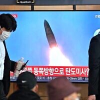 People walk past a television screen showing a news broadcast with file footage of a North Korean missile test, at a railway station in Seoul on October 4, 2022. (Jung Yeon-je/AFP)