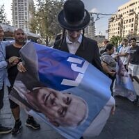 An ultra-Orthodox man holds a poster bearing a portrait of former prime minister and Likud party leader Benjamin Netanyahu, during a Likud party campaign rally on October 20, 2022, at the Mahane Yehuda market in Jerusalem ahead of the November general elections. (MENAHEM KAHANA / AFP)
