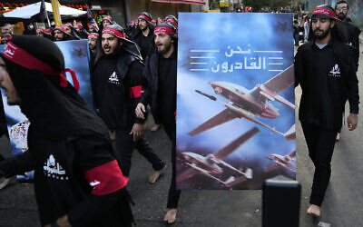 Shiite Lebanese members of Iranian-backed Hezbollah walk barefoot as they carry a poster showing Hezbollah drones with Arabic words that reads: "We are coming," during the holy day of Ashoura in a southern suburb of Beirut, Lebanon, Tuesday, Aug. 9, 2022. (AP/Hussein Malla)