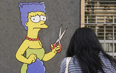 A woman takes pictures of a mural called 'The Cut' by street artist aleXsandro Palombo depicting Marge Simpson, a character of the animated television series 'The Simpsons,' cutting her iconic hair, in front of the Consulate of Iran, in Milan, Italy, October 5, 2022. (AP Photo/Luca Bruno)