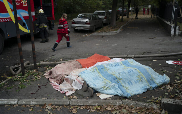 A member of the rescue service walks past three bodies, covered by blankets, following a Russian attack in Dnipro, Ukraine, October 10, 2022. (AP Photo/Leo Correa)