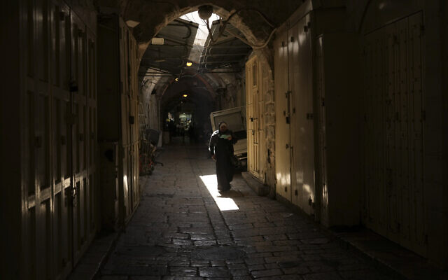 A woman walks past shuttered shops in Jerusalem's Old City on October 12, 2022. (AP Photo/Mahmoud Illean)