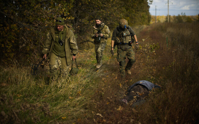 Ukrainian territorial defence deminers walk past a body of a local man who was killed after an explosion of a Russian mine near Hrakove village, Ukraine, October 13, 2022. (AP Photo/Francisco Seco)