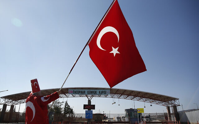 Illustrative: A man holding a Turkish flag stands at the Oncupinar border crossing with Syria, Jan. 28, 2018. (AP Photo/Lefteris Pitarakis)