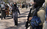Afghan women pass next to a Taliban fighter in Kabul, Afghanistan, February 13, 2022. (AP Photo/Hussein Malla)