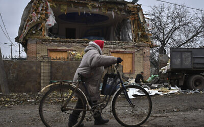 A woman passes with a bicycle as a local resident works to clean the debris from a damaged house after Russian shelling in Kramatorsk, Ukraine, Thursday, Nov. 10, 2022. (AP Photo/Andriy Andriyenko)