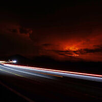In this long camera exposure, cars drive down Saddle Road as Mauna Loa erupts in the distance, Monday, Nov. 28, 2022, near Hilo, Hawaii. Mauna Loa, the world's largest active volcano erupted Monday for the first time in 38 years. (AP Photo/Marco Garcia)