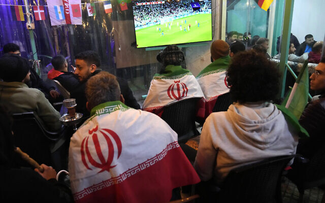 Lebanese soccer fans of Iran's team cover their backs with Iranian flags, as they sit at a coffee shop smoking water pipes and watch the World Cup group B soccer match between Iran and the United States, in the Hezbollah stronghold in the southern suburbs of Beirut, Lebanon, Tuesday, Nov. 29, 2022. (AP/Hussein Malla)