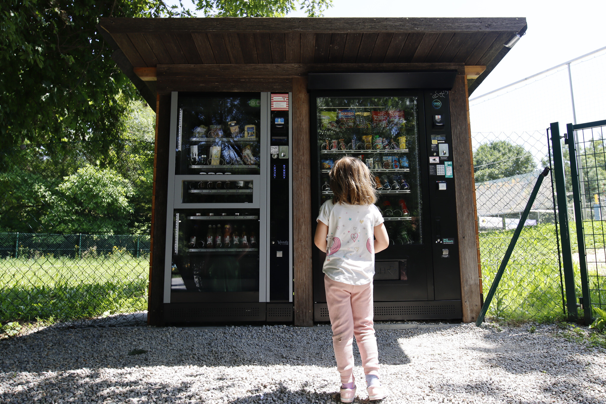 Lily, daughter of Amy Feineman, stops at a vending machine on her way home from school in Graz, Austria, on June 27, 2022. The refrigerated vending machine on the left offers items such as sausage, cheese, eggs and drinks from local businesses. (Raquel G. Frohlich)