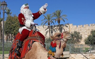 Issa Kassissieh, dressed as Santa Claus, poses for a picture as he rides a camel at Jaffa Gate in Jerusalem's Old City on December 2, 2022 (AHMAD GHARABLI / AFP)