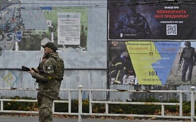 A Ukrainian policeman speaks on his phone next to a poster (R, up) calling on residents to denounce those who collaborated with the Russian forces during their occupation of the city, Kherson, December 8, 2022, (Genya SAVILOV/AFP)