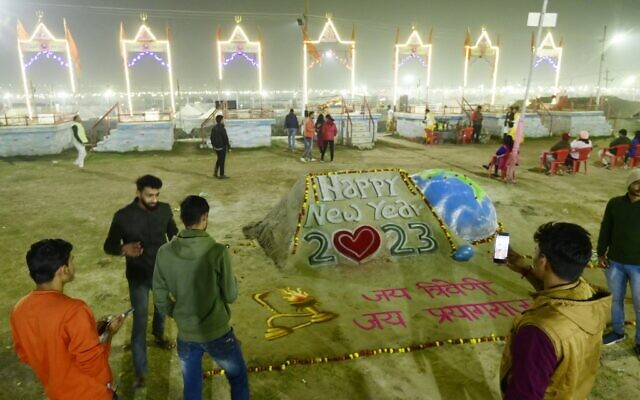 People take pictures near a sand sculpture for New Year at the Sangam area, the confluence of the rivers Ganges, Yamuna and mythical Saraswati, in Prayagraj, India, on December 31, 2022. (Sanjay Kanojia/AFP)