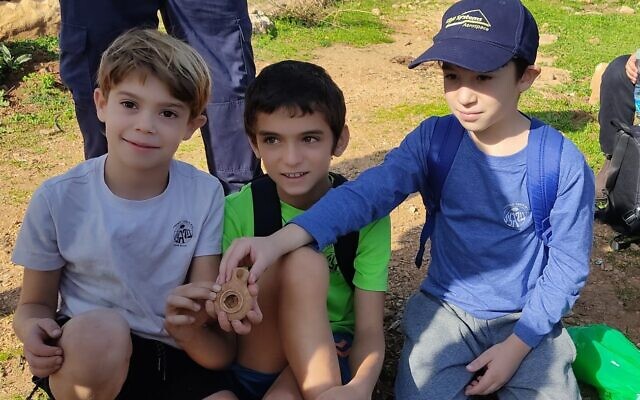 Grade four students Alon Cohen, Liam Atias, and Rotem Levnat with an ancient oil lamp they discovered in Kibbutz Parod, December 2022. (Israel Antiquities Authority)