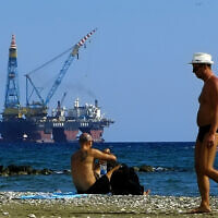 Illustrative: People on a beach as a drilling platform is seen in the background outside from Larnaca port, in the eastern Mediterranean island of Cyprus, October 15, 2017. (Petros Karadjias/AP)