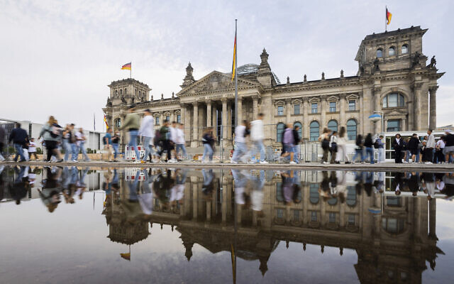 People walk past the Reichstag building while being reflected in a puddle in Berlin, Germany, September 6, 2022. (AP/Christoph Soeder)