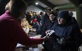 A woman receives medicine boxes from a volunteer at a heating tent at a a government-built help station, in Kherson, Ukraine, December 3, 2022. (Evgeniy Maloletka/AP)